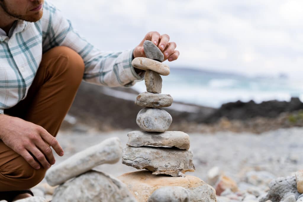 Man doing Zen balanced stones stack on beach